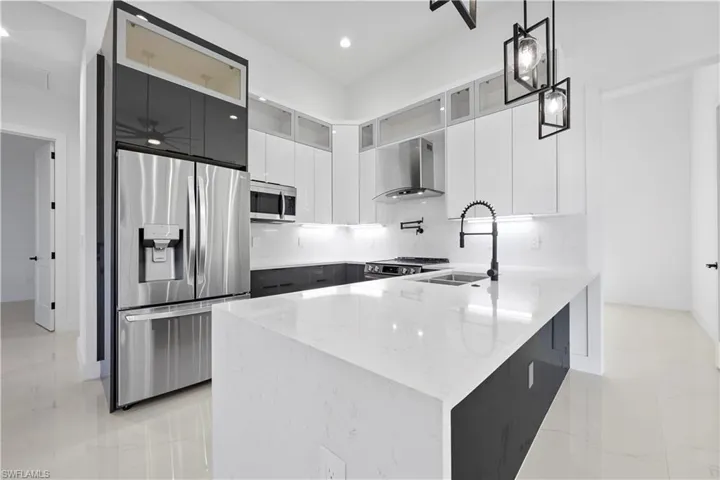 Kitchen featuring a sink, light stone counters, appliances with stainless steel finishes, a peninsula, and wall chimney range hood