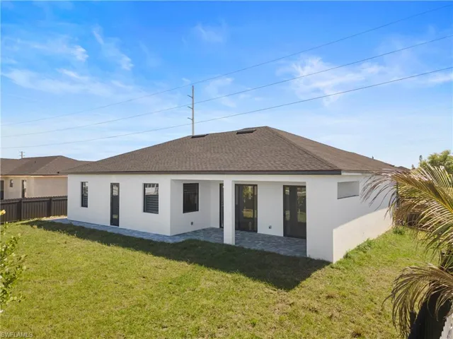 Back of property featuring fence, stucco siding, a shingled roof, a patio area, and a lawn