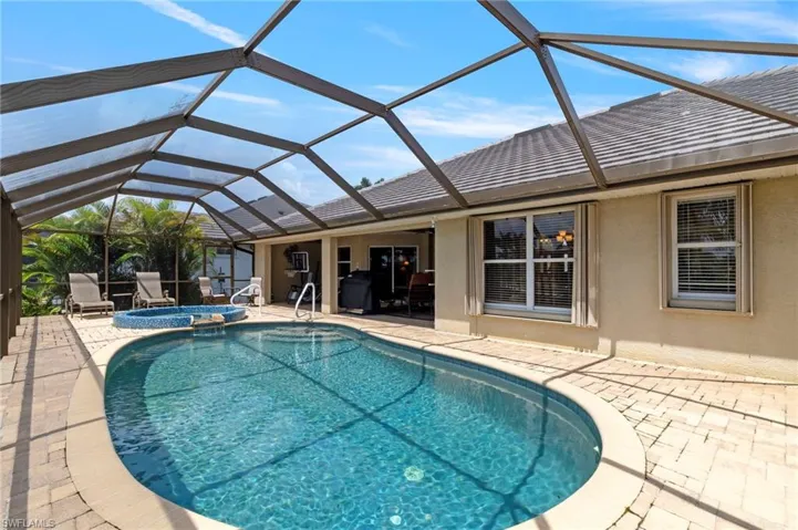 View of pool with a patio area, a pool with connected hot tub, and glass enclosure