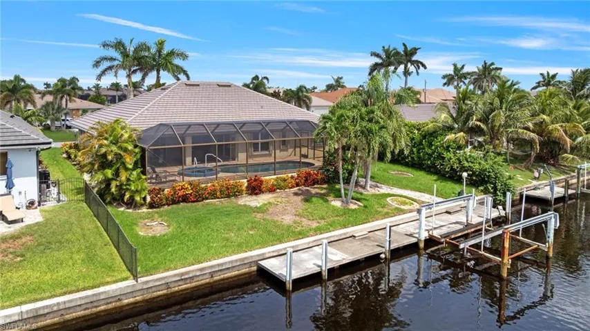 Rear view of property with boat lift, a water view, a yard, a tile roof, and glass enclosure