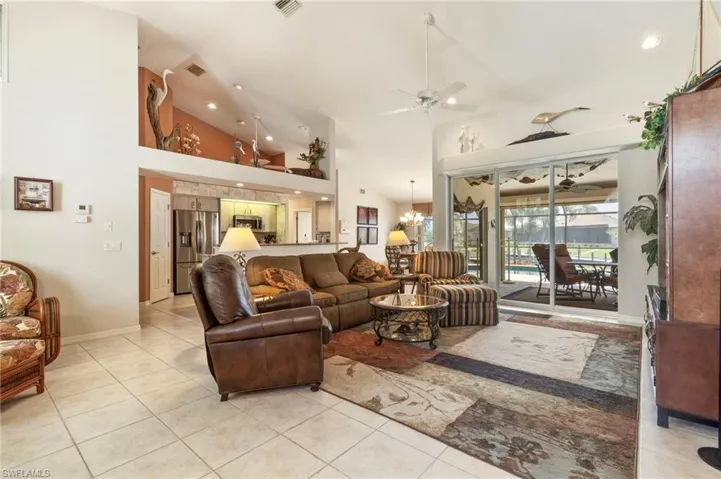 Living area with ceiling fan, light tile patterned flooring, high vaulted ceiling, recessed lighting, and a chandelier