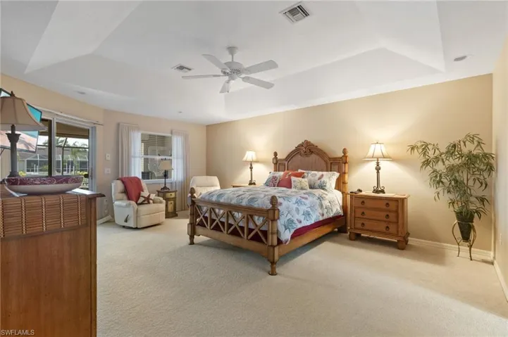 Bedroom featuring light colored carpet, a tray ceiling, access to exterior, and a ceiling fan