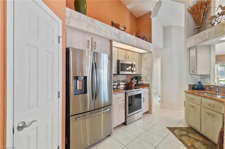 Kitchen featuring appliances with stainless steel finishes, light brown cabinets, light tile patterned floors, stone countertops, and a towering ceiling