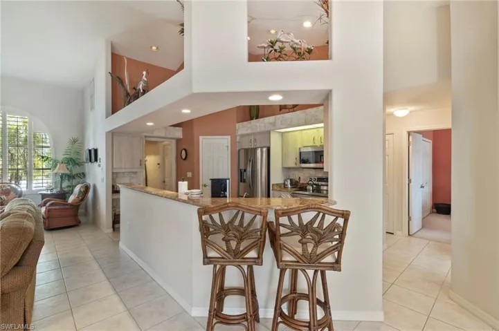 Kitchen with light tile patterned flooring, appliances with stainless steel finishes, a high ceiling, a kitchen breakfast bar, and open floor plan