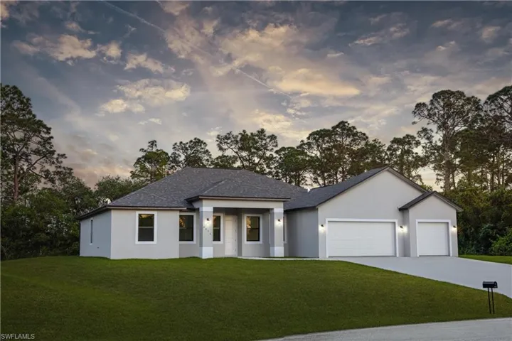 The property features a gray exterior with white trim, a dark gray shingled roof, a paved driveway, and an expansive green lawn