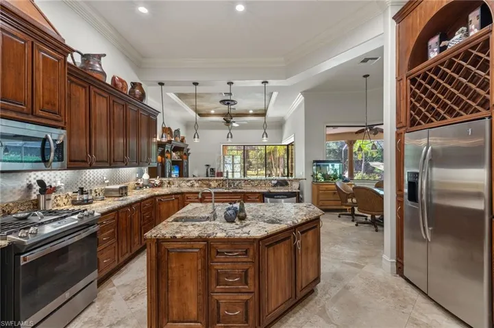 Kitchen featuring kitchen peninsula, an island with sink, stainless steel appliances, hanging light fixtures, and a soaring ceiling