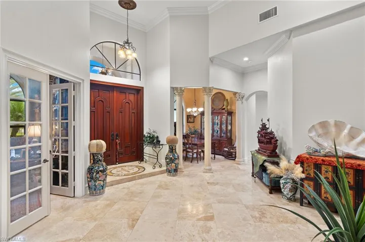 Entryway with Marble Tile, crown molding, decorative columns, a chandelier, and a towering ceiling.