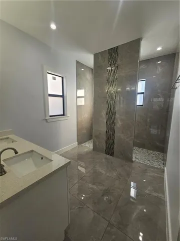 Bathroom with walk in shower, double vanity, plenty of natural light, marble tiled flooring, and recessed lighting