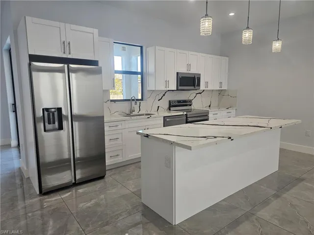 Kitchen with stainless steel appliances, light stone counters, white cabinetry, light marble finish flooring, and a kitchen island