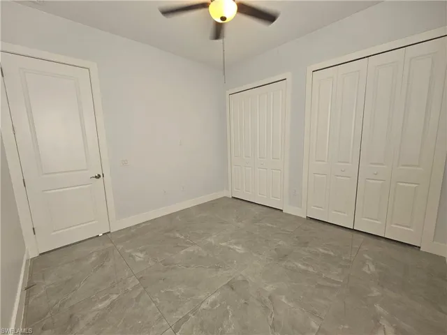 Unfurnished bedroom with multiple closets, a ceiling fan, and light marble finish floors