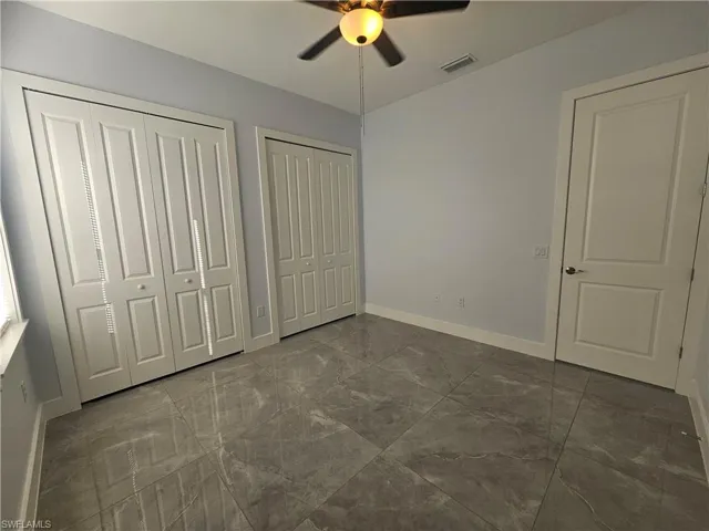 Unfurnished bedroom featuring multiple closets, ceiling fan, and dark marble finish flooring