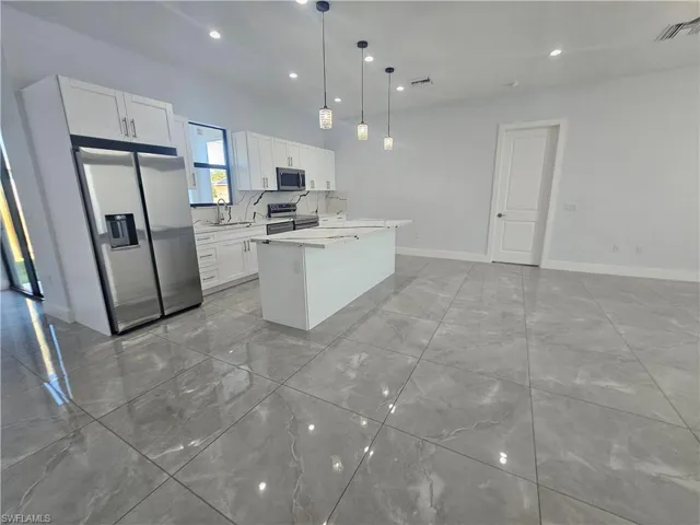 Kitchen with stainless steel appliances, a kitchen island, decorative light fixtures, white cabinets, and light stone countertops
