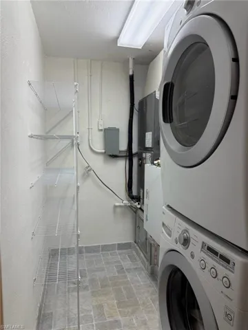 Washroom featuring stacked washer / drying machine and tumbled marble floors