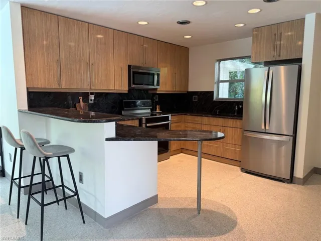 Kitchen with a peninsula, stainless steel appliances, a kitchen breakfast bar, recessed lighting, and granite backsplash