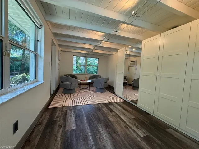 Large game room area with laminate wood finished floors, a wood ceiling with exposed beams, and a separate AC through-wall unit
