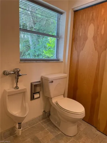 Hall guest bathroom featuring toilet, a urinal and tumbled marble floors