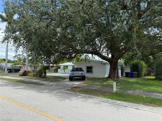 View of front of house featuring large paver driveway, a front yard, and mature landscaping