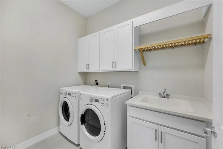 Laundry area with light tile patterned floors, cabinets, sink, and washer and dryer