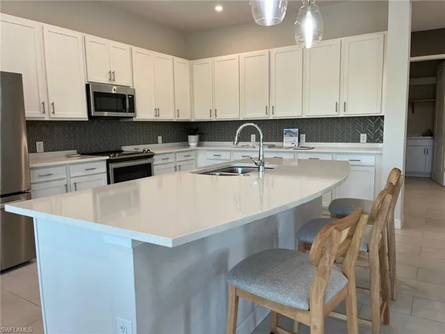 Kitchen with tasteful backsplash, a kitchen breakfast bar, a sink, light tile patterned floors, and stainless steel appliances