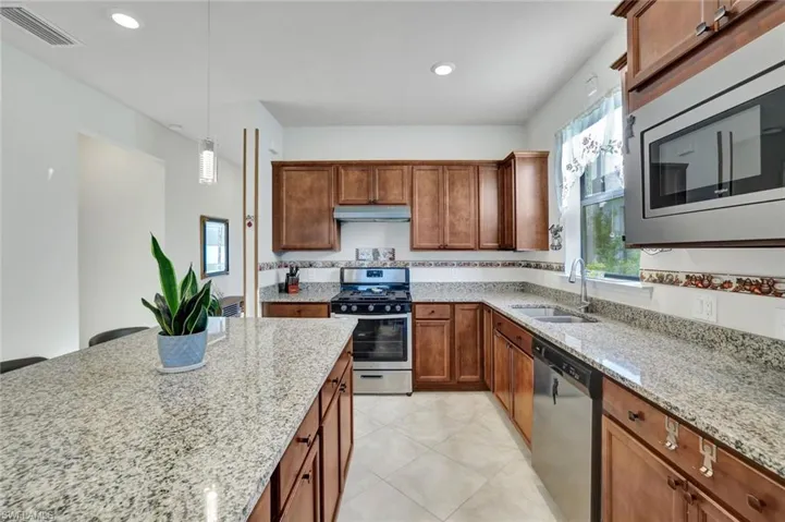 Kitchen featuring stainless steel appliances, hanging light fixtures, brown cabinets, light stone countertops and recessed lighting
