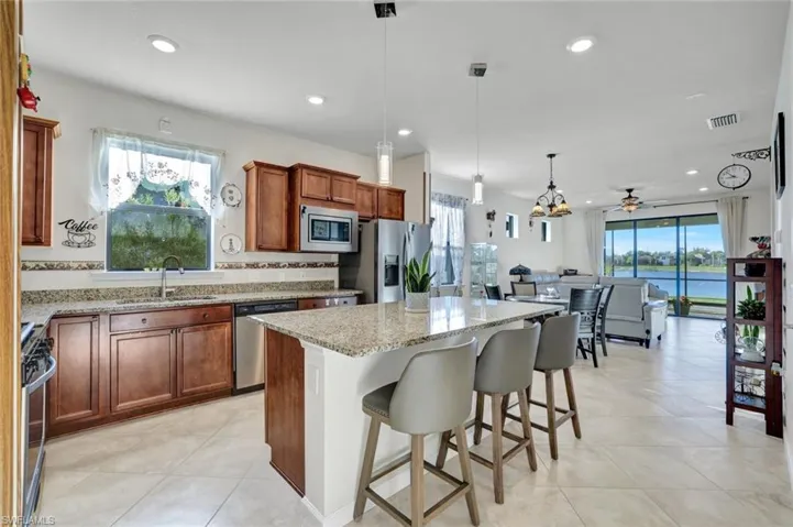 Kitchen featuring brown cabinetry, decorative light fixtures, a kitchen island, breakfast bar and plenty of natural light