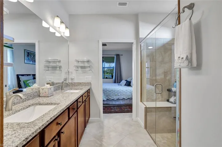 Ensuite bathroom with double vanity, a stall shower, and light tile patterned floors