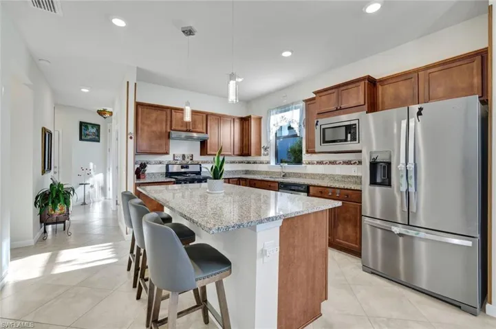Kitchen with stainless steel appliances, brown cabinets, decorative light fixtures, light stone countertops, and recessed lighting