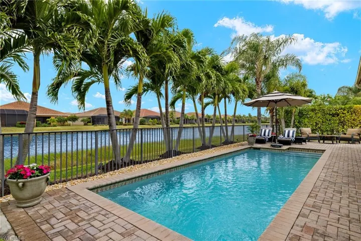 View of custom salt water, solar heated swimming pool ,an outdoor living space, an extended lanai and a sunset water view. Upgrades include mature Palms and landscape lighting and extended lanai.