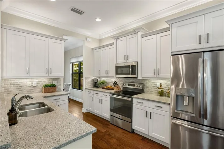 Kitchen with light stone countertops, custom tiled backsplash,sink, white cabinets, and stainless steel appliances