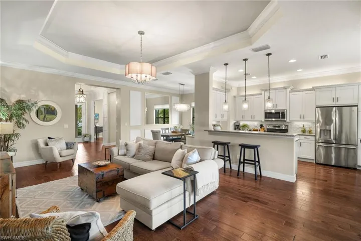 Open Great room featuring dark hardwood / wood floors, a raised tray ceiling, ornamental crown molding, and a decorator chandelier