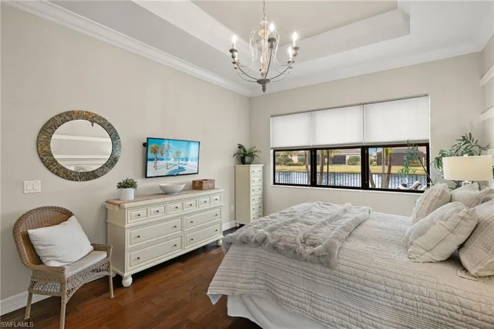 Bedroom featuring a raised tray ceiling, crown molding, dark wood-type flooring, and a notable chandelier