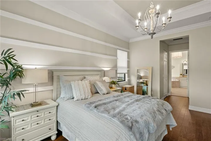 Bedroom with ensuite bathroom, dark hardwood flooring, ornamental molding, and an inviting chandelier and custom wall detailing.