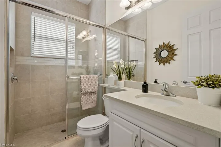 Bathroom with tiled shower to ceiling, window, patterned flooring, plenty of natural light, vanity.