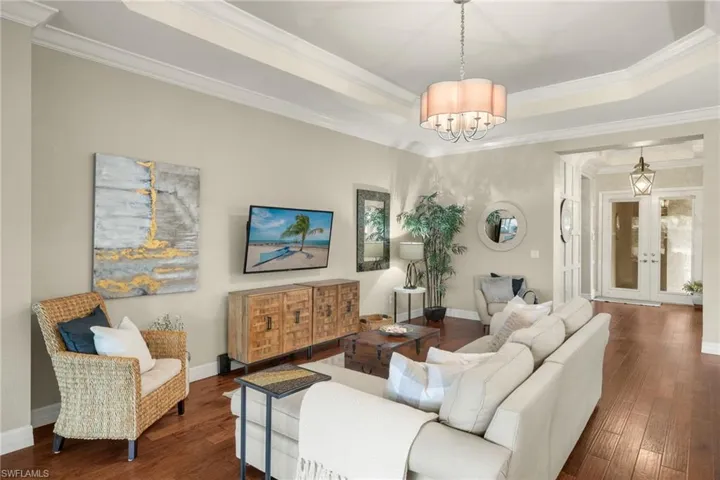 Open Bright and Sunny great room featuring french doors entry, a raised tray ceiling, crown moulding, an inviting chandelier, and dark hardwood / wood floors