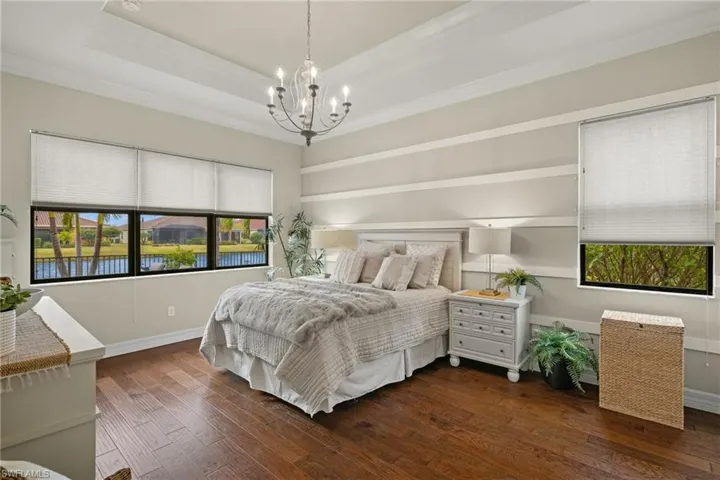 Bedroom featuring a tray ceiling, crown molding, a sunset water view, an inviting chandelier, and dark hardwood floors