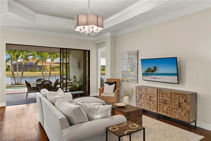 Great room with hardwood floors, an inviting chandelier, a raised tray ceiling, sunset water view, and ornamental crown molding