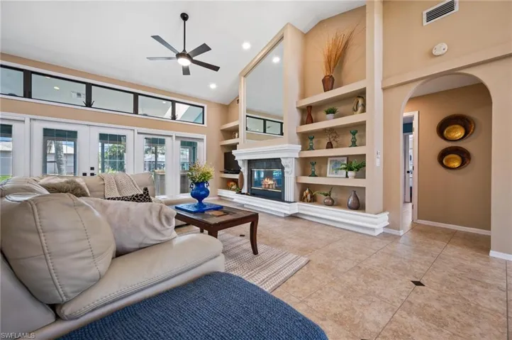 Living area featuring high vaulted ceiling, a ceiling fan, built in shelves, light tile patterned flooring, and arched walkways