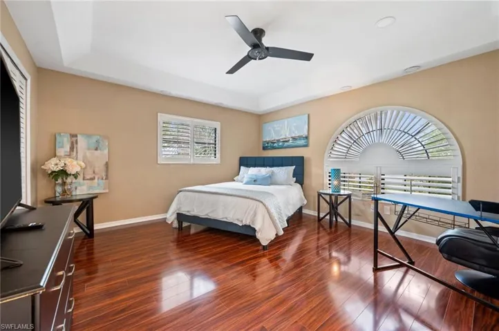 Bedroom featuring wood finished floors, a tray ceiling, baseboards, and a ceiling fan