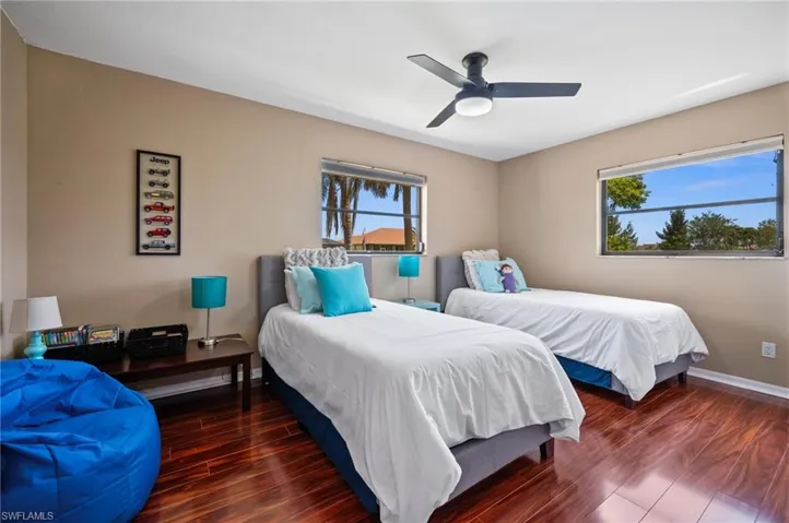 Bedroom with multiple windows, wood finished floors, a ceiling fan, and baseboards