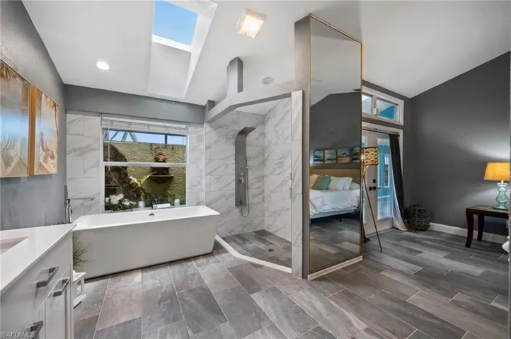 Ensuite bathroom featuring vaulted ceiling, a freestanding bath, tiled shower, and vanity