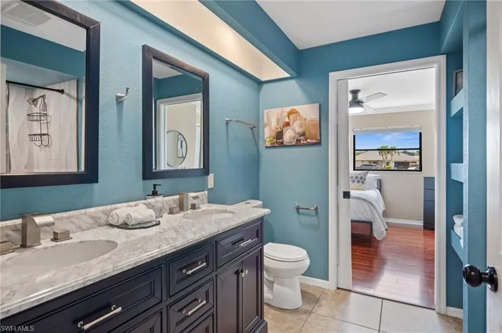 Bathroom featuring double vanity, toilet, tile patterned flooring, ceiling fan, and baseboards