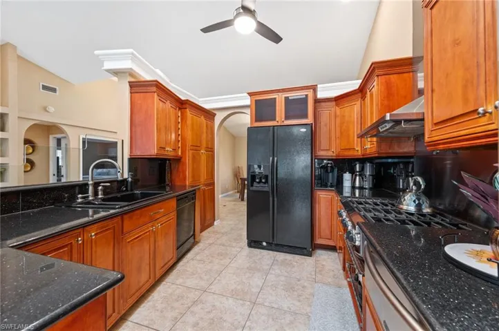 Kitchen with black appliances, a sink, arched walkways, ceiling fan, and wall chimney range hood