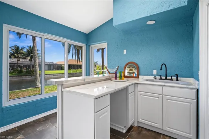 Kitchen featuring a textured wall, lofted ceiling, a sink, healthy amount of natural light, and a water view