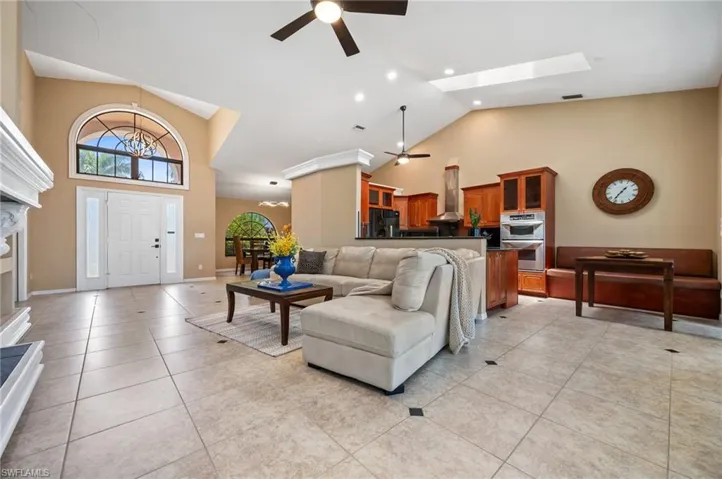 Living room featuring ceiling fan, high vaulted ceiling, a fireplace, light tile patterned floors, and recessed lighting