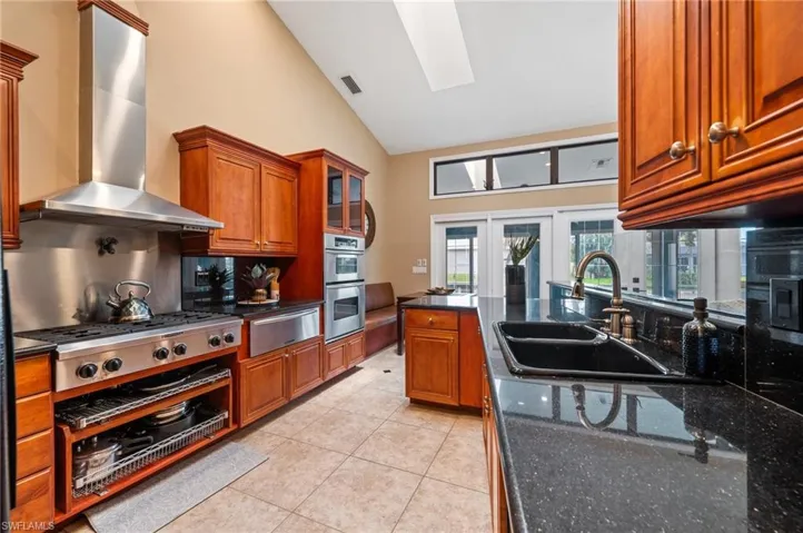 Kitchen with wall chimney exhaust hood, a warming drawer, a skylight, appliances with stainless steel finishes, and a sink