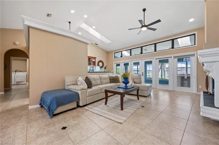 Living room featuring ceiling fan, arched walkways, light tile patterned floors, a high ceiling, and recessed lighting