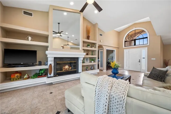 Living room featuring ceiling fan, high vaulted ceiling, built in features, tile patterned floors, and a glass covered fireplace