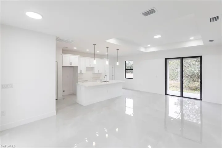 Kitchen with decorative light fixtures, white cabinets, a raised ceiling, and a kitchen island with sink