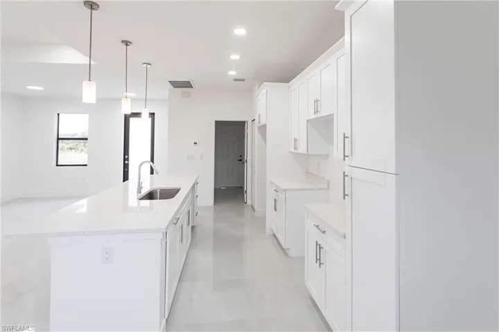 Kitchen featuring white cabinets, an island with sink, light stone countertops, and sink