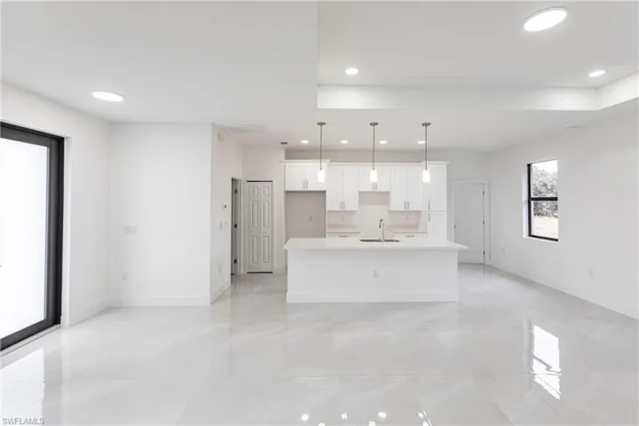 Kitchen with sink, pendant lighting, white cabinets, and a kitchen island with sink